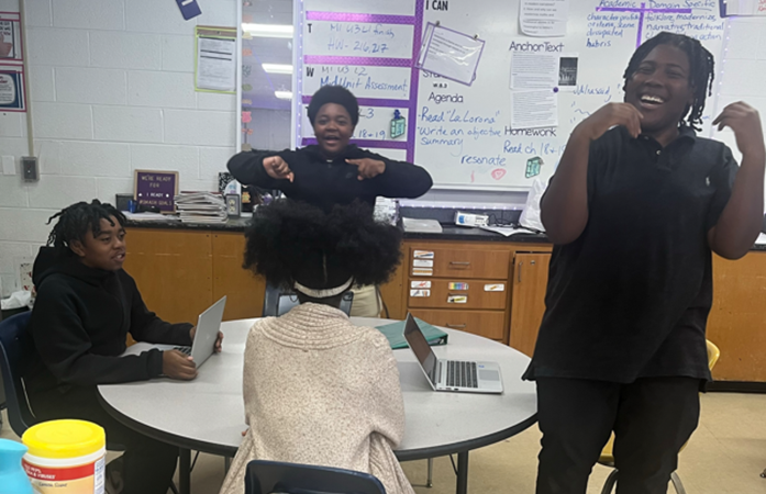  2 students standing looking excited and 2 students sitting talking